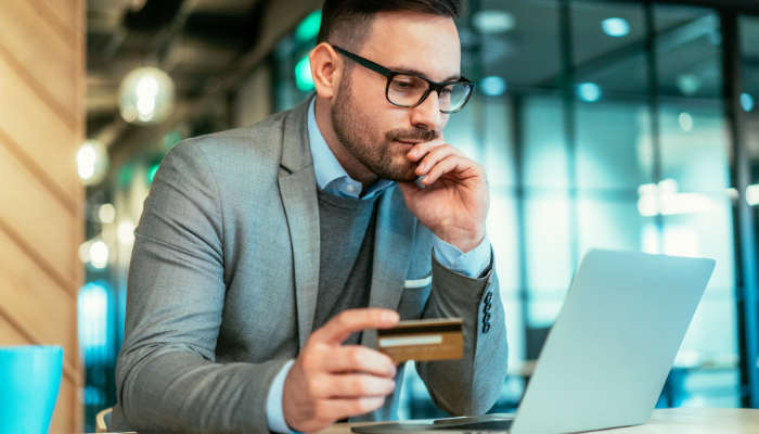 Business owner holding a payment card while reviewing a laptop before making an upfront business payment
