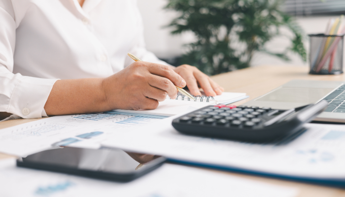 Person reviewing business paperwork, notes, and a calculator while managing outgoing expenses