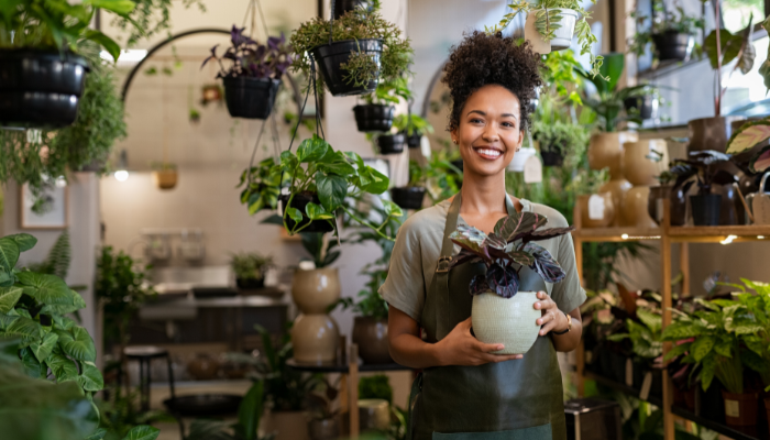 Small business owner smiling and holding a potted plant inside her plant shop.