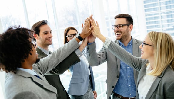 Group of business professionals smiling and giving a team high-five, symbolizing strong collaboration and shared success between financial partners.