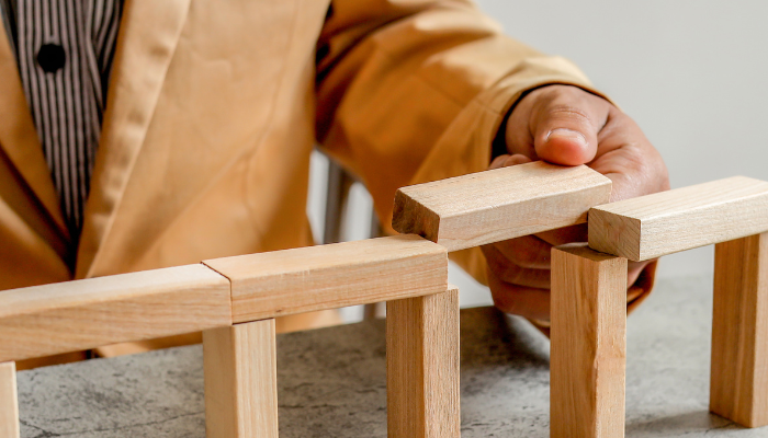 Hands placing wooden blocks to bridge gaps, symbolizing solutions for cash flow timing issues