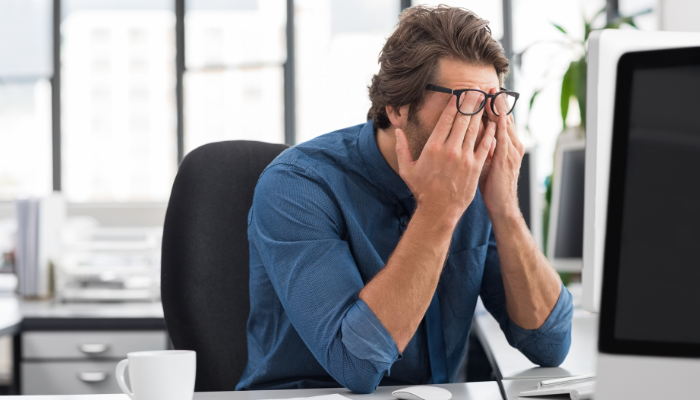 Banker sitting at his desk with his hands over his face, showing the pressure financial institutions are under as clients struggle with cash-flow challenges