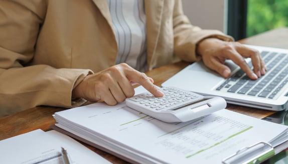 Hands using a calculator over invoices and spreadsheets to reconcile receivables