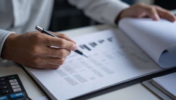 Close-up of hands analyzing financial documents and budget projections with a pen.