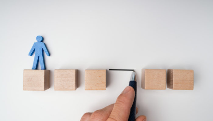 Hand drawing a line between wooden blocks to help a small figure bridge a gap, symbolizing support for borrowers who are close to qualifying for bank credit.