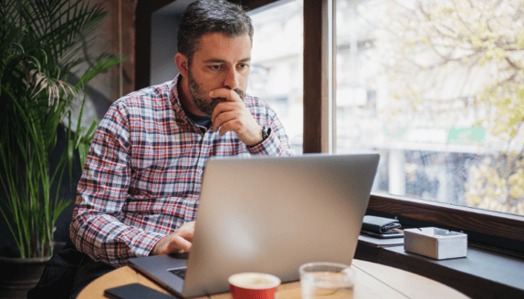 Business owner focused on laptop, reviewing financial or funding options in a café setting.