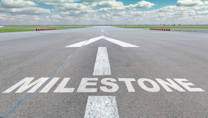 Arrow pointing forward with the word 'Milestone' painted on an empty road, representing business progress and financial goals.