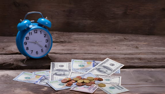 Alarm clock next to cash and coins representing delayed payments and cash flow timing pressure