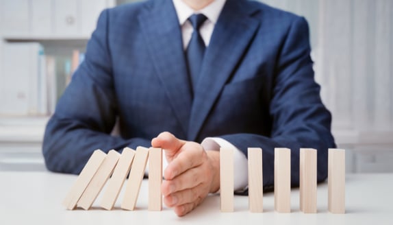 Business leader stopping falling domino blocks symbolizing financial stability and risk management during rising costs.