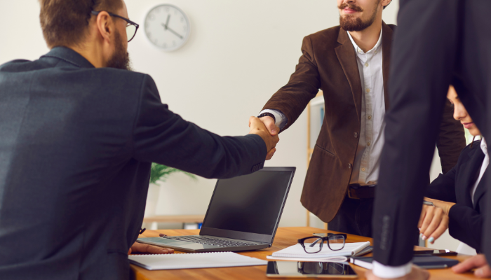 Two professionals shaking hands over a desk in a business setting, representing trust in financial partnerships.
