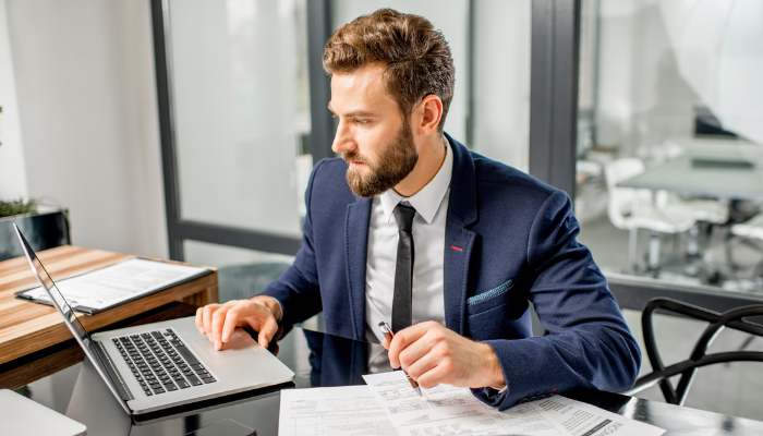 Business owner reviewing financial documents and working on a laptop to manage cash flow and business operations.