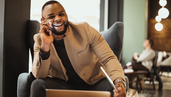 Entrepreneur smiling on phone with laptop, discussing flexible funding options