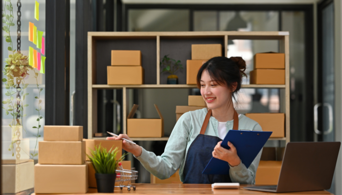 Small business owner managing inventory in a workspace, smiling and holding a clipboard.