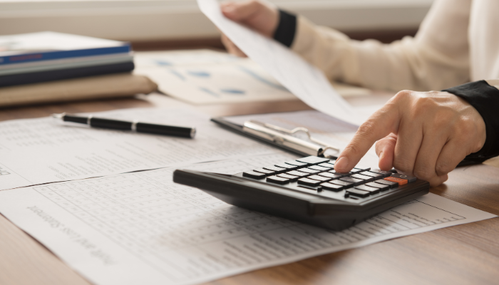 Business owner using calculator to review unpaid invoices and financial statements at desk