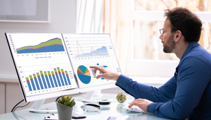 Business owner analyzing financial charts and data on dual monitors reviewing financing and cash flow trends