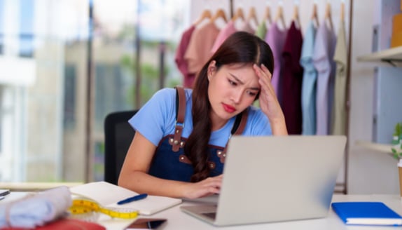 Small business owner stressed at laptop in her boutique worried about cash flow and business finances