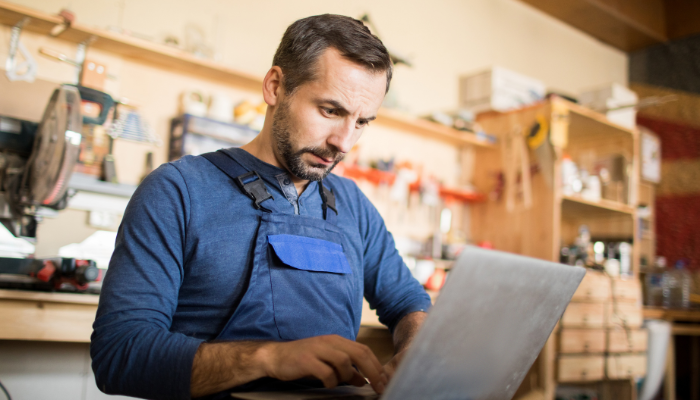 Trade business owner in workshop focused on laptop managing his own business finances and operations