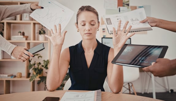 Overwhelmed business professional at a desk surrounded by charts, paperwork, and competing demands
