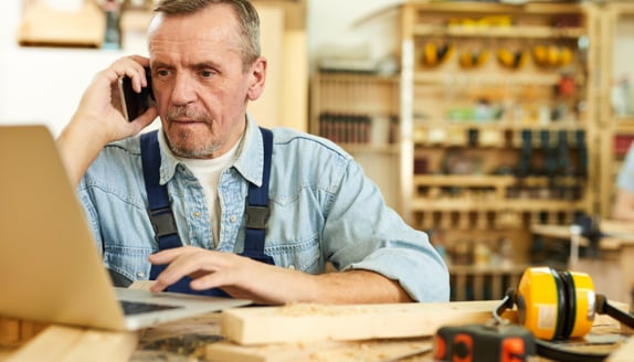 Small business owner in workshop on phone researching invoice factoring options for his company