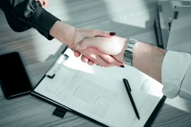 Two professionals shaking hands over financial documents, representing agreement on invoice factoring terms.