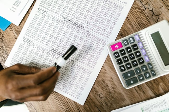 Top-down view of a person reviewing financial spreadsheets with a pen beside a calculator on a wooden desk.