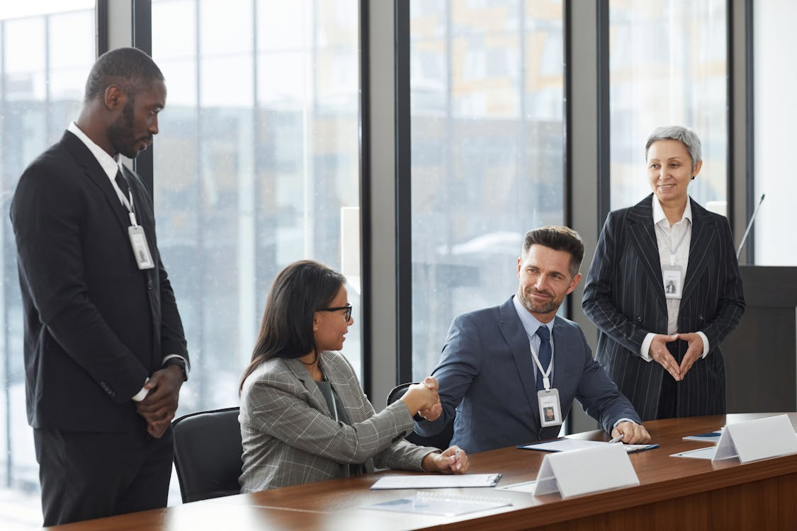 Business professionals in a meeting shaking hands across a conference table, representing successful financial partnership and business growth.