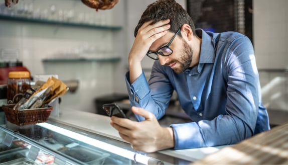Business owner checking a phone with concern while waiting on incoming payments