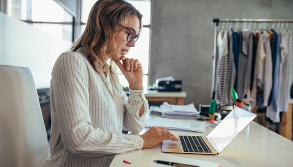 Businesswoman reviewing information on a laptop while managing growing work demands and expenses